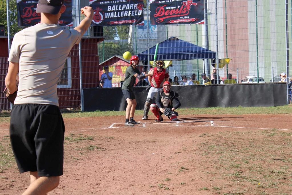 Pitcher von hinten beim Wurf, im Hintergrund Batter und Catcher