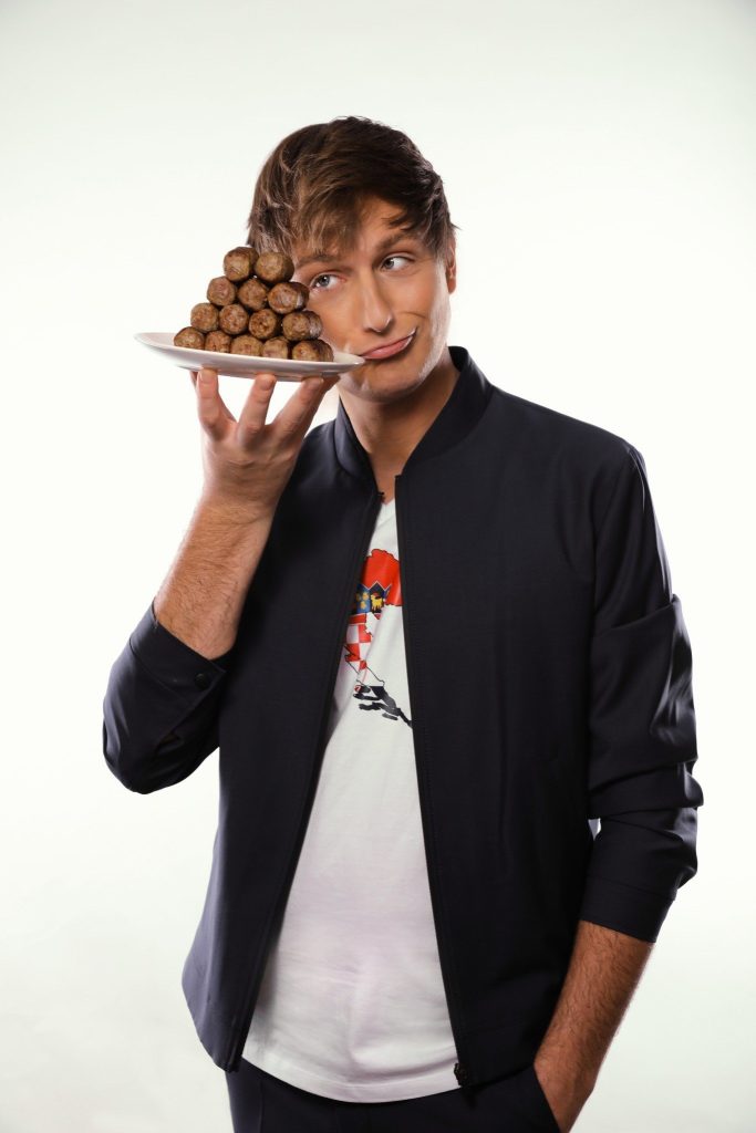 Comedian Boris Stijelja hält einen Teller mit Cevapcici neben sein Gesicht