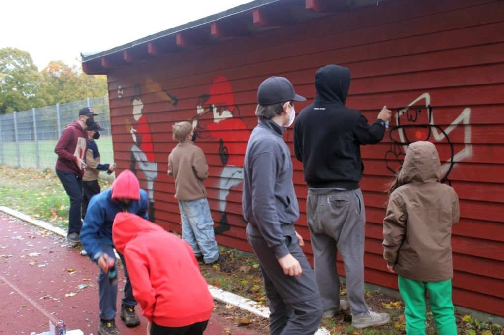 Gruppe von Kindern und Erwachsenen sprayt an der Wand eines roten Baseball-Hauses