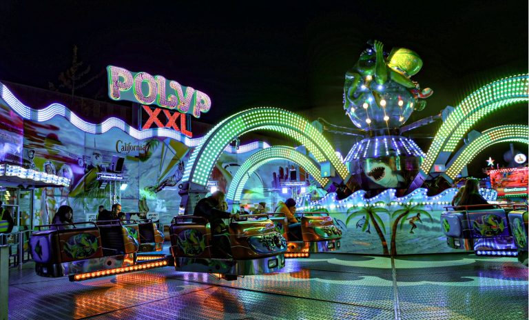 Beleuchtetes Kirmes-Fahrgeschäft „Polyp XXL“ bei Nacht mit grünen Lichtbögen