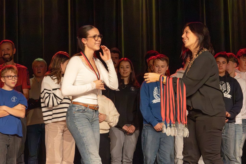 Bürgermeisterin hängt einer jungen Sportlerin auf der Bühne eine Medaille um, im Hintergrund weitere Geehrte