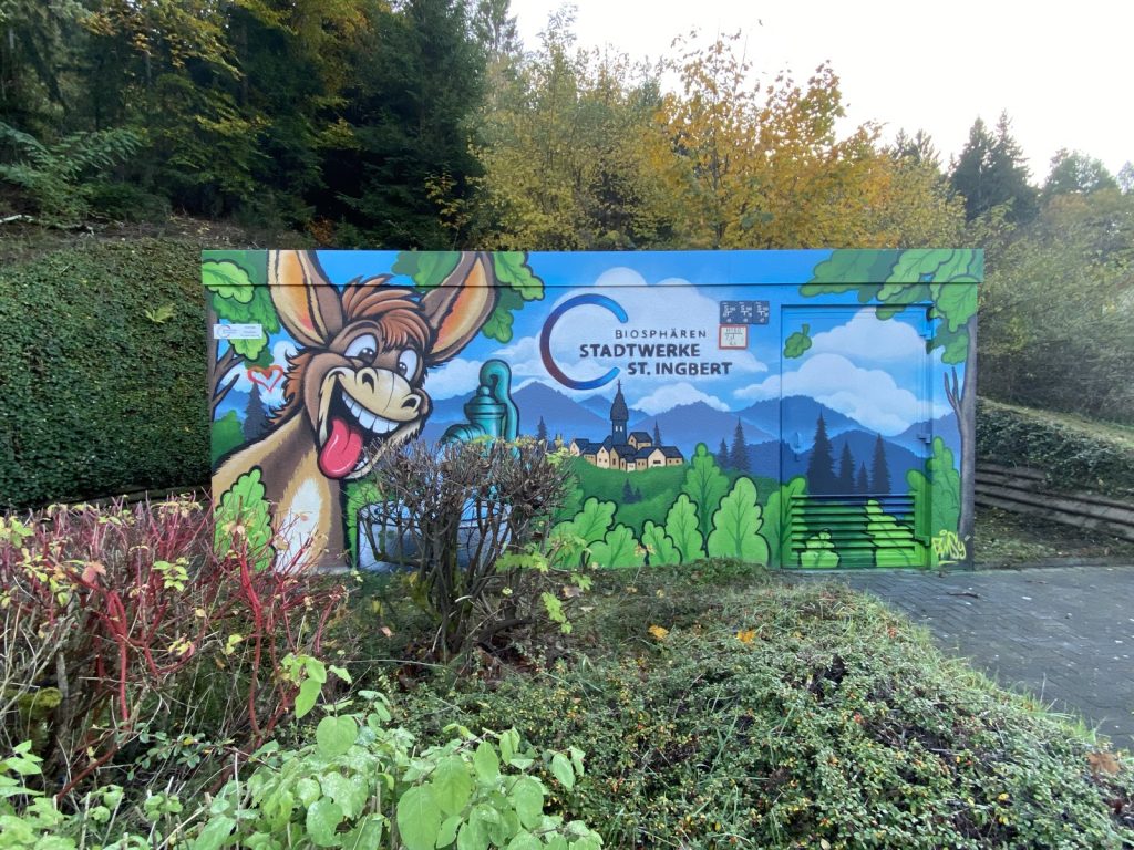 Mit Graffiti gestaltete Trafostation in Oberwürzbach: grinsender Maulesel, Eselbrunnen, Landschaft und Logo der Biosphären Stadtwerke St. Ingbert